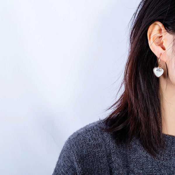 Pendientes de botón de acero inoxidable y titanio con forma de corazón y concha blanca.