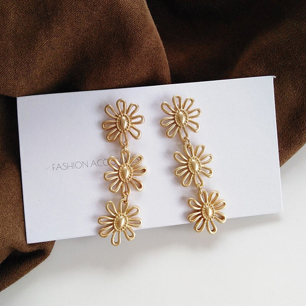 Pendientes de clip con textura de color oro mate, de metal, pequeños y sencillos, con flores de margaritas largas.